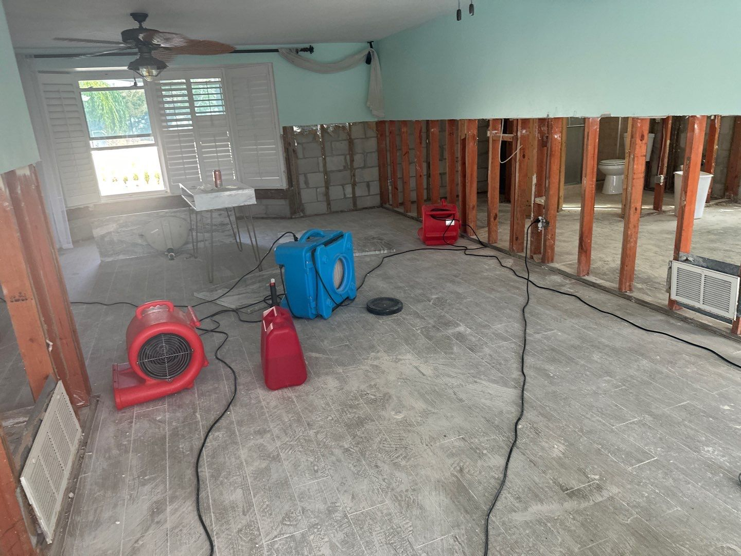 Air movers and drying equipment inside a flood damaged home with exposed wall framing during water mitigation